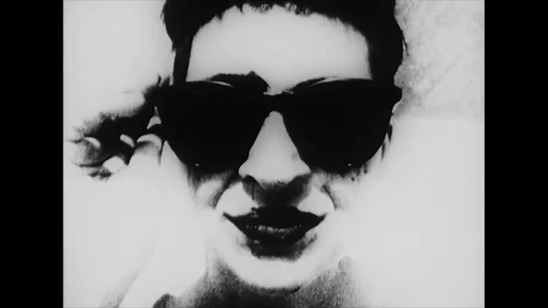 Schwarz-weiße Werkabbildung eines frontal dargestellten Gesichts mit Sonnenbrille. Eine Hand berührt den Brillenrand; die Darstellung ist stark kontrastiert