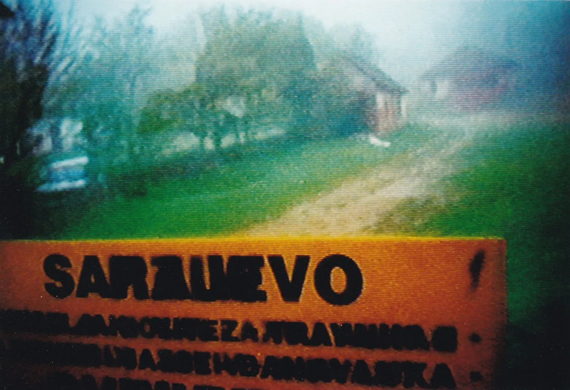 Warnschild im Vordergrund, dahinter Bauernhäuser, Straße, Wiese, Bäume