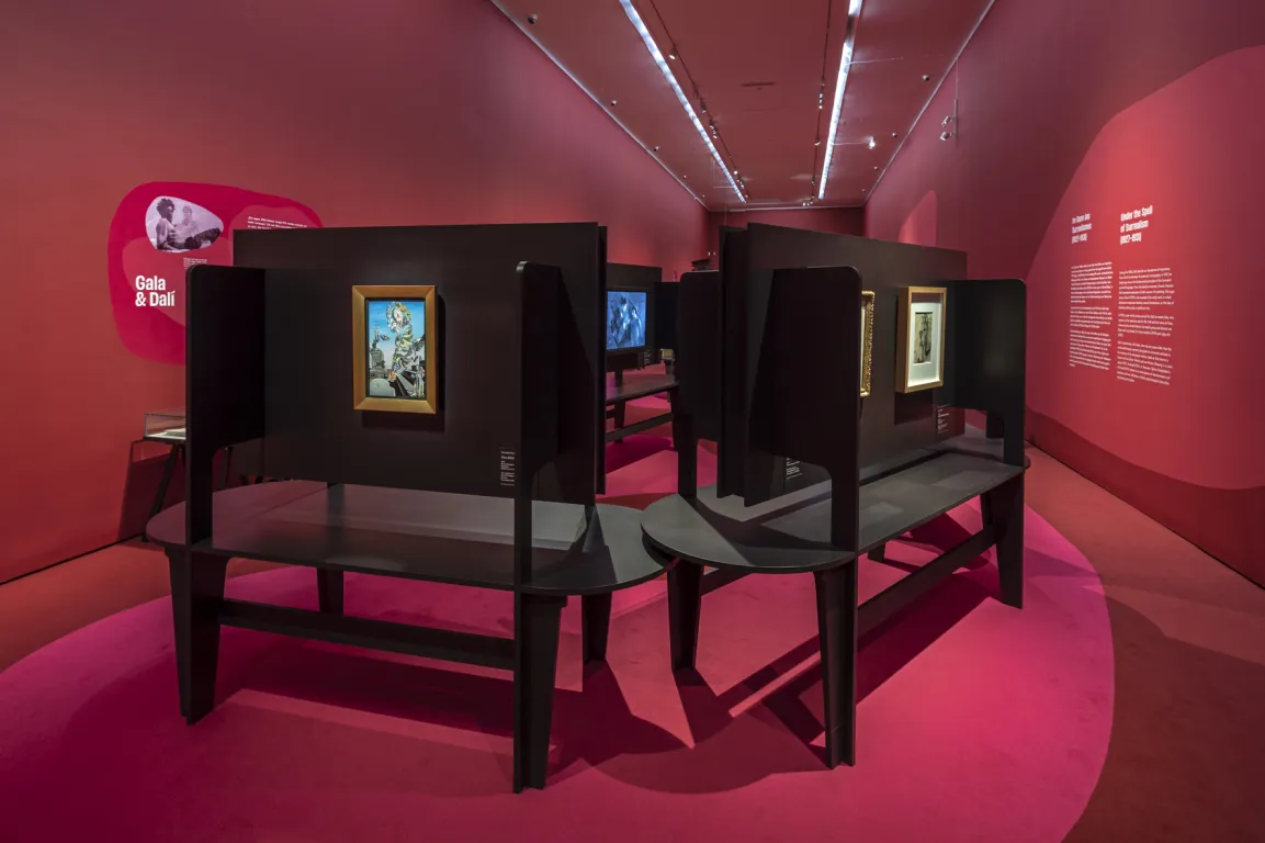 Ausstellungsraum mit roten Wänden, darauf surrealistische Bilder 