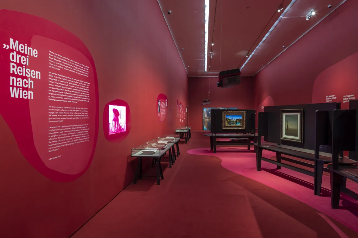 Ausstellungsraum mit roten Wänden, darauf surrealistische Bilder 