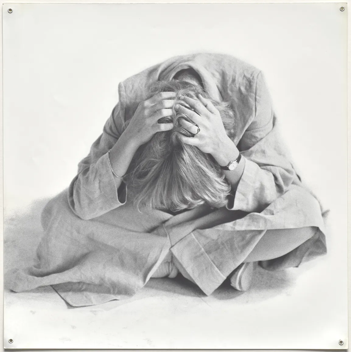 Schwarzweißfotografie einer jungen Frau auf dem Boden kauernd, den Körper krampfhaft gebeugt, den Kopf fest umklammert 