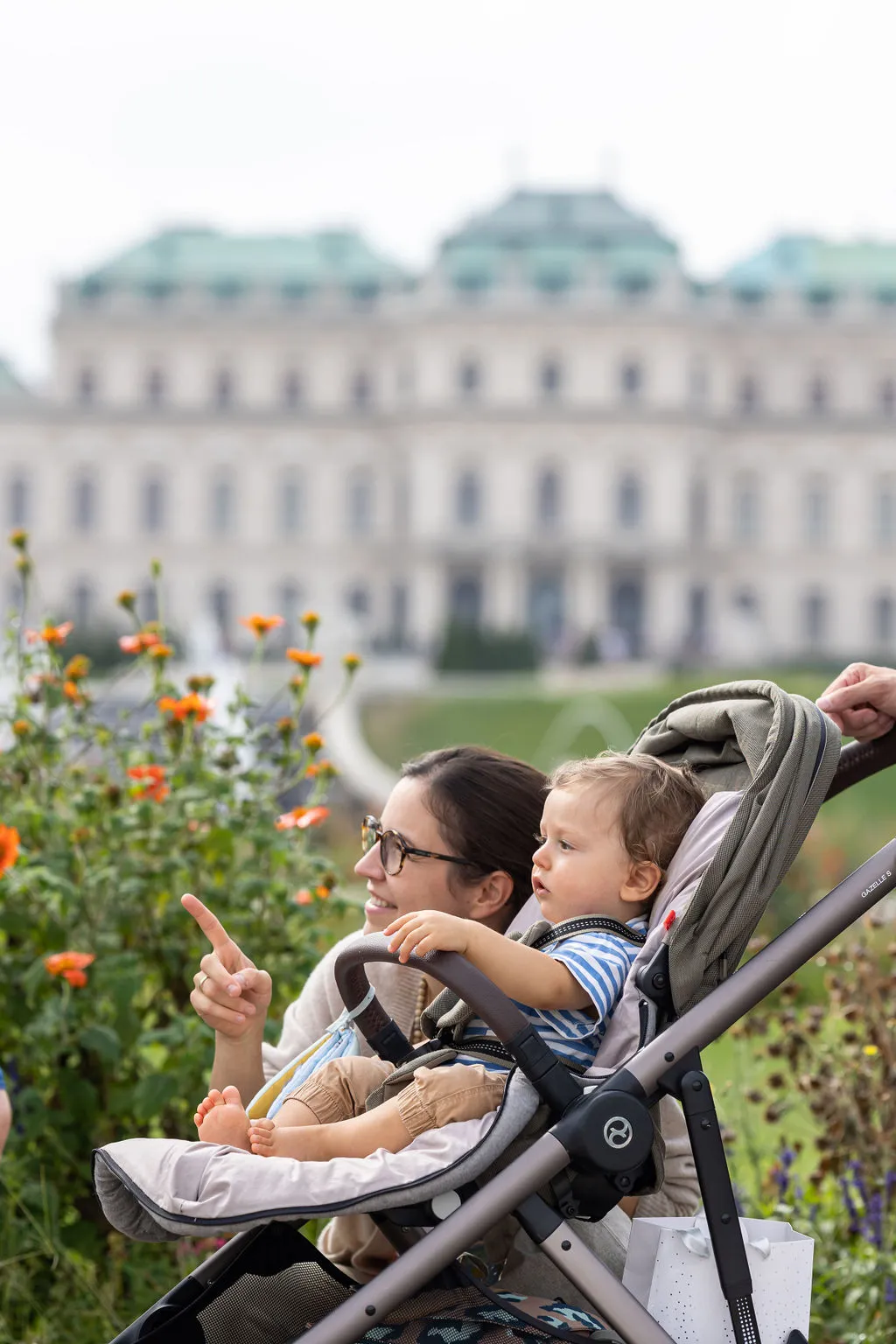 Eine Mutter zeigt ihrem Kind im Kinderwagen etwas im Schlosspark. Im Hintergrund ist das Barockschloss Oberes Belvedere zu sehen.