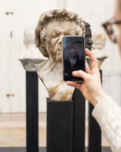 Eine Frau macht mit dem Handy Fotos von einem Charakterkopf von Franz Xaver Messerschmidt im Ausstellungsraum