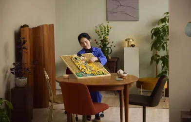 A woman assembling the LEGO® Art set Gustav Klimt – The Kiss while seated at a table.