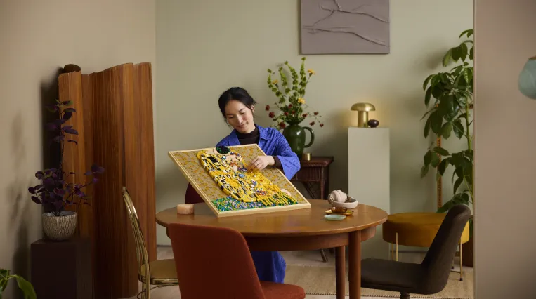 Eine Frau, an einem Tisch sitzend, baut das LEGO Art Set von Gustav Klimts "Der Kuss" zusammen